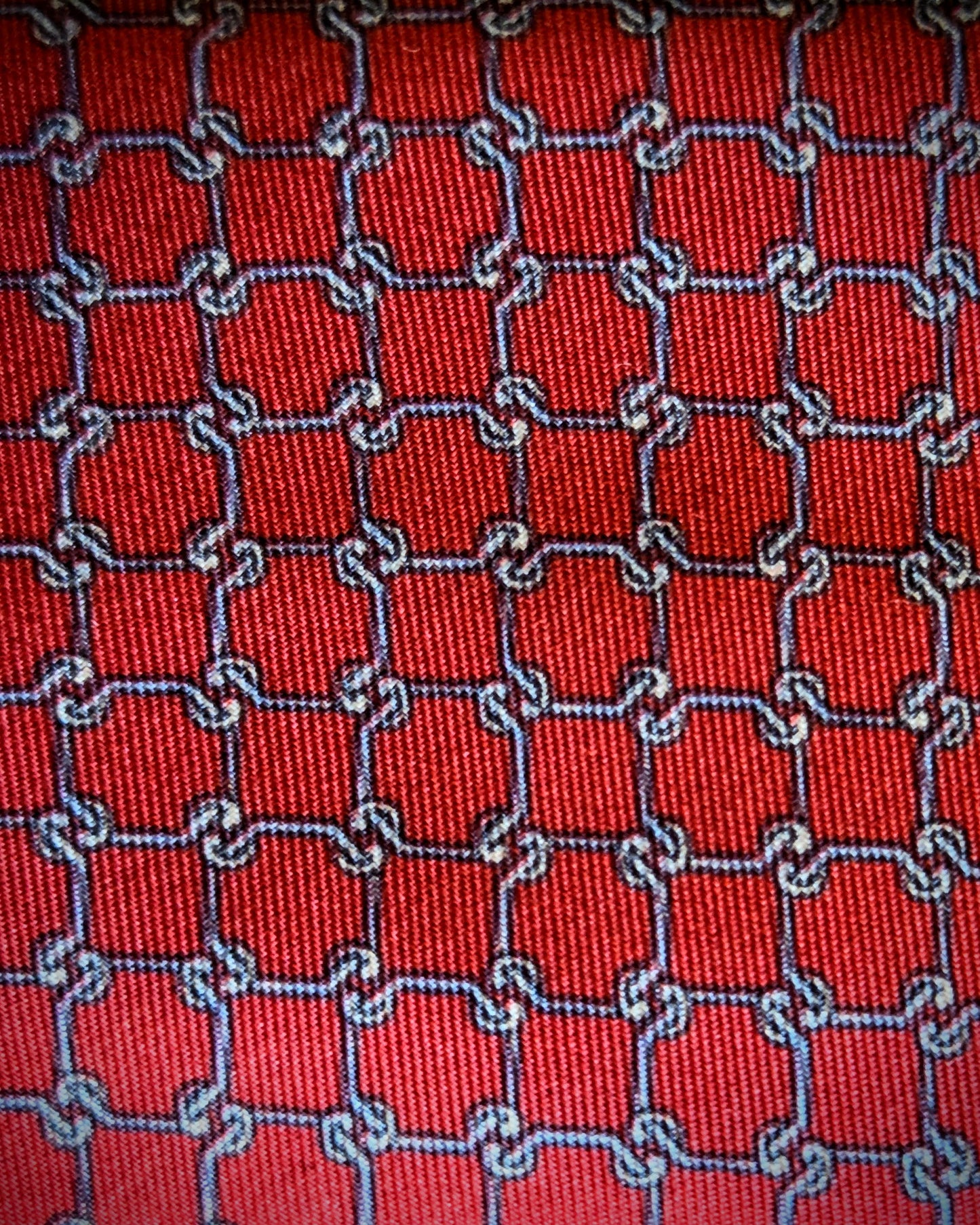 A close-up of a red woven fabric with a repeating interlocking chain pattern outlined in blue and white.