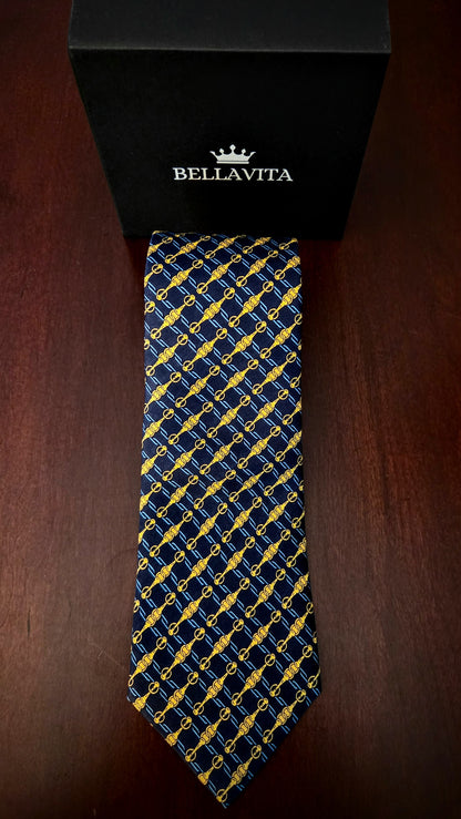 A Bellavita necktie with a navy blue and yellow geometric pattern, displayed vertically in front of its black branded gift box on a dark wooden surface.