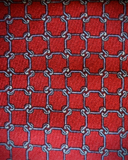 A close-up of a red woven fabric with a repeating interlocking chain pattern outlined in blue and white.