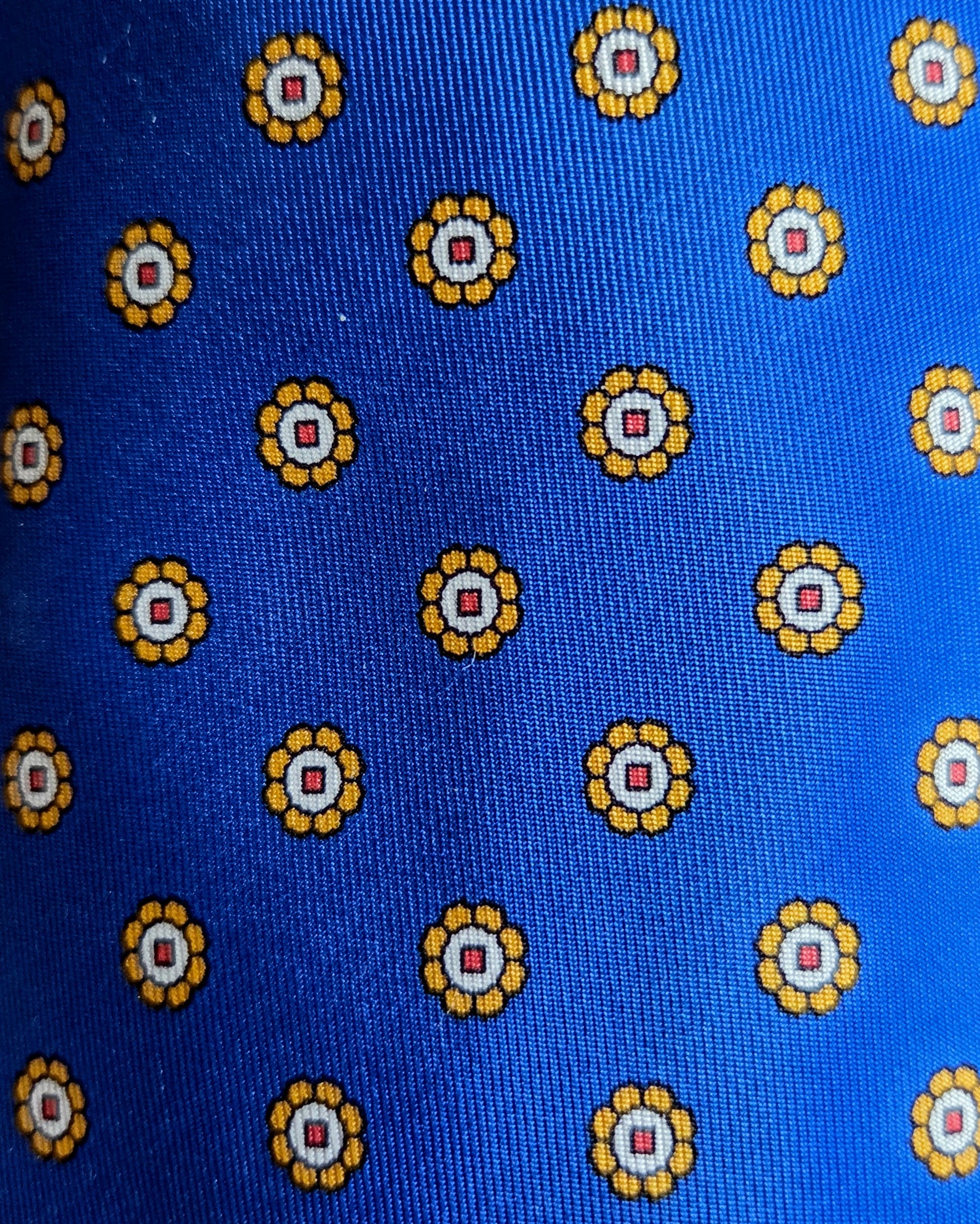 A close-up of a blue fabric with a repeating pattern of yellow and white circular medallions.