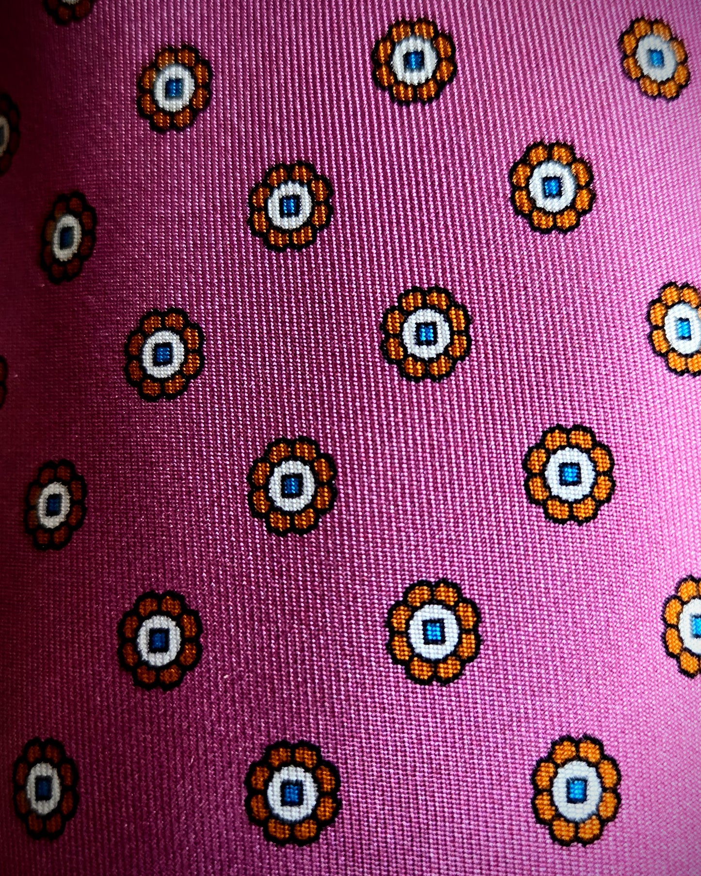 A close-up of a pink woven fabric with a repeating circular floral pattern in orange, white, and blue.