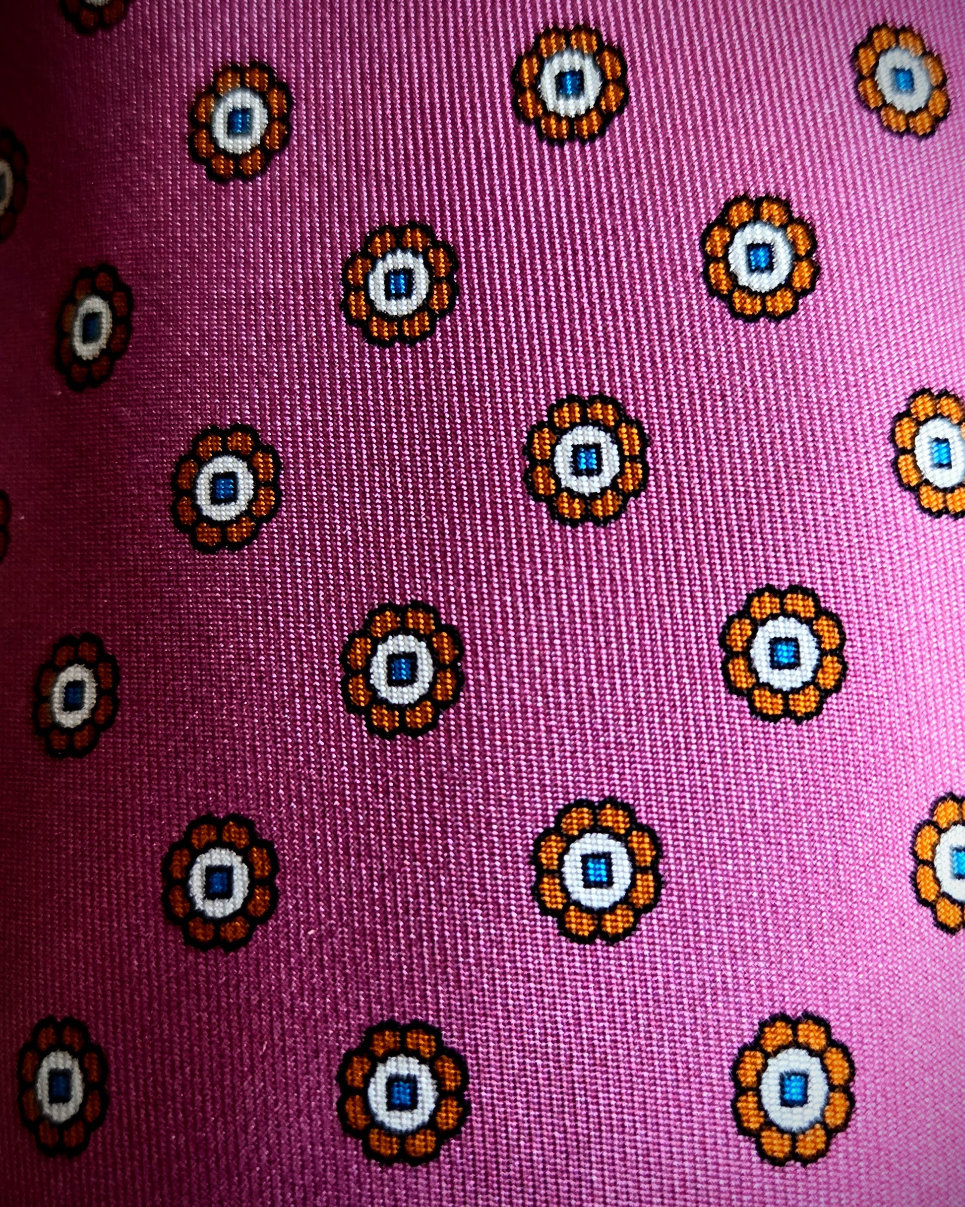A close-up of a pink woven fabric with a repeating circular floral pattern in orange, white, and blue.