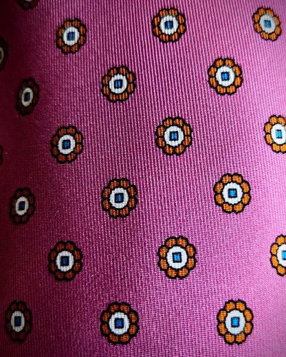 A close-up of a pink woven fabric with a repeating circular floral pattern in orange, white, and blue.