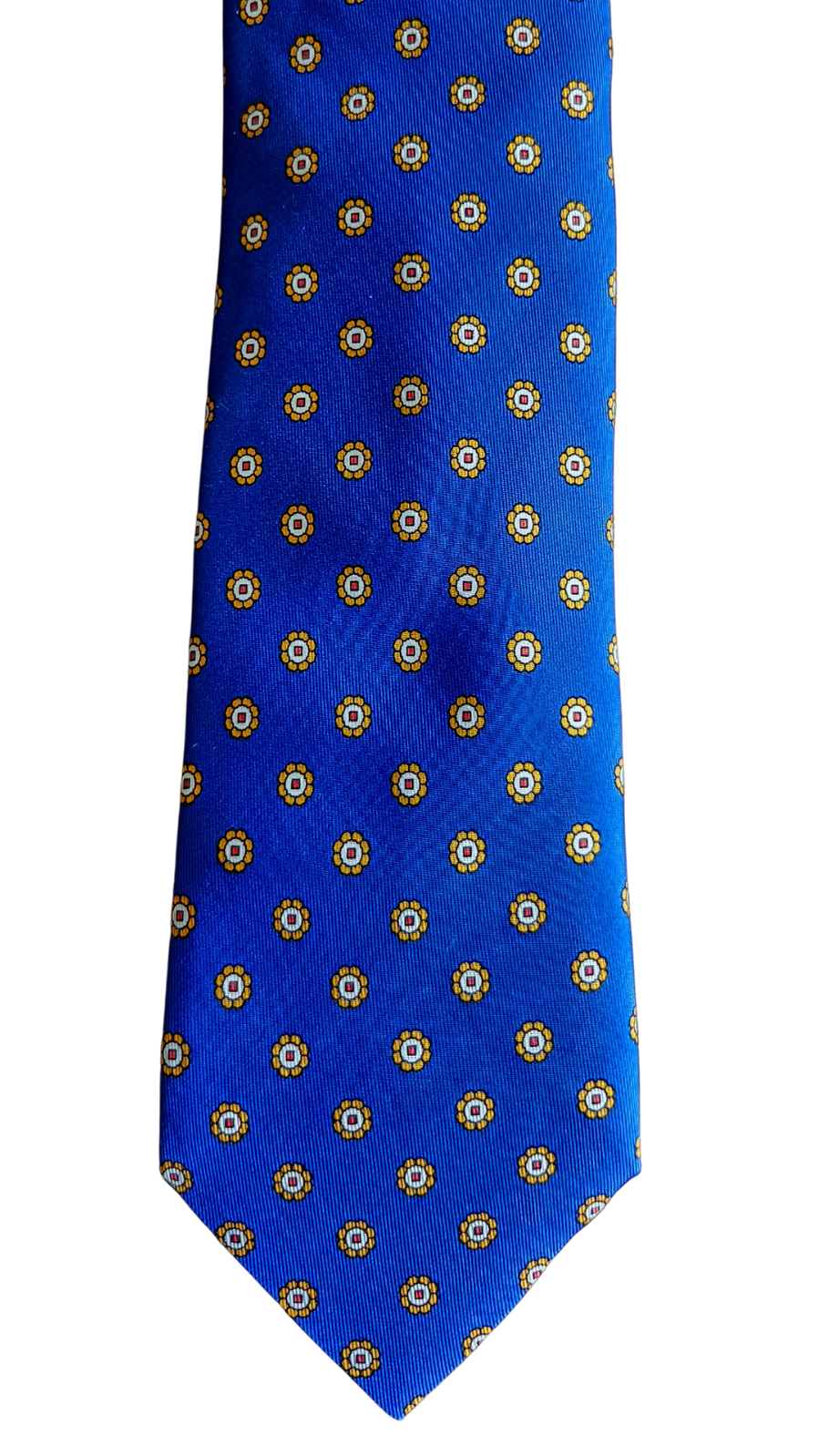 A royal blue necktie with a repeating pattern of small gold and white geometric medallions, shown flat against a plain white background.